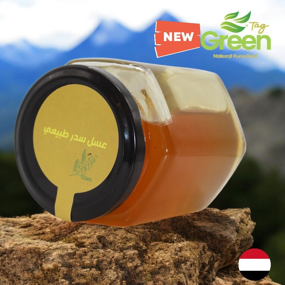 أفضل نوع عسل للطاقة: اكتشف السر في عسل السدر الطبيعي 1 جرة زجاجية سداسية الشكل لعسل سدر يمني تحمل عبارة “عسل سدر طبيعي”، موضوعة على جانبها فوق صخرة ويظهر في الخلفية جبال شاهقة.