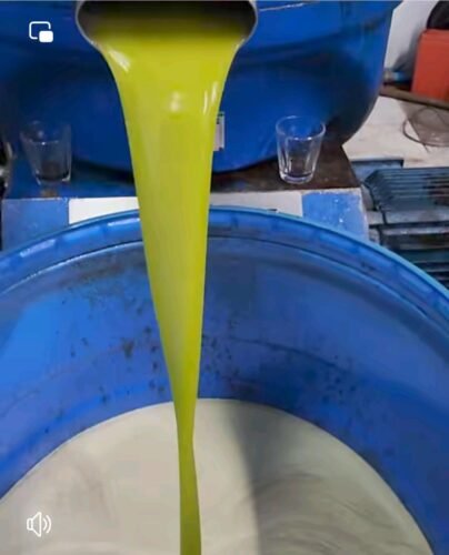 زيت زيتون نقي وطازج يتدفق من العصارة إلى برميل أزرق في معصرة زيتون.