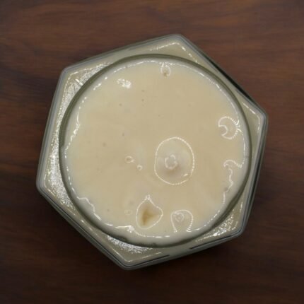 Top-down view of Raw Uzbek White Mountain Honey in a hexagonal glass jar on a wooden background